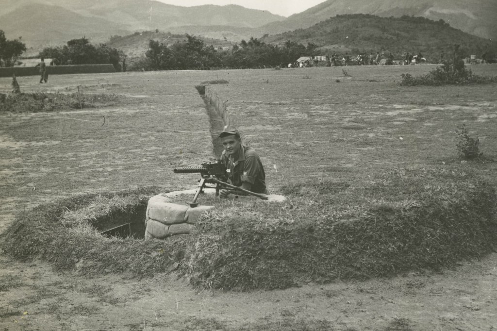 Image: A soldier stationed with Grant Townsend stands behind a gun while stationed in Vietnam.