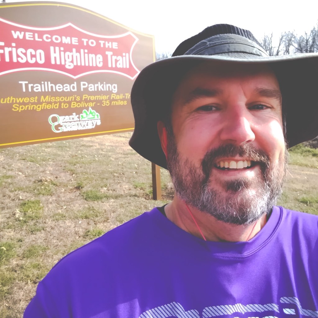 Mark Applegate standing in front of a sign welcoming people to the Frisco Highline Trail, which connects Springfield, Missouri, to Bolivar, Missouri.