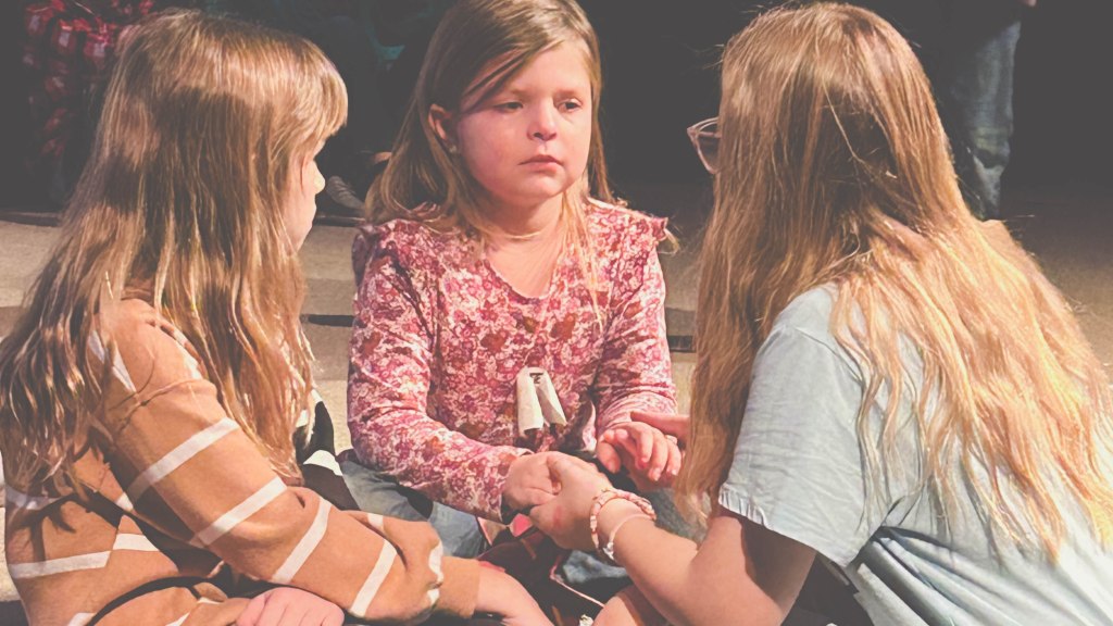 Two young girls speaking and comforting another young girl who had been crying and praying at a church in southwest Missouri. The girl with glasses is holding hands with the girl who had been crying.