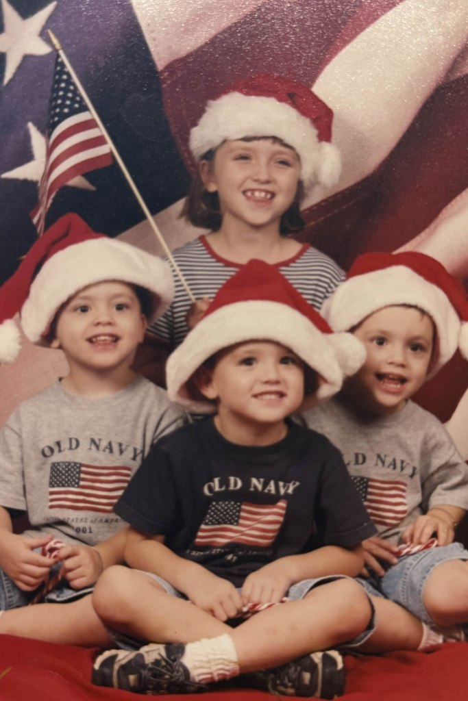 As kids, Kaleigh Steward, Benjamin Steward, Alec Steward and Jakob Steward dressed in red, white and blue Old Navy outfits, while sitting in front of an American flag, with Santa Claus hats.